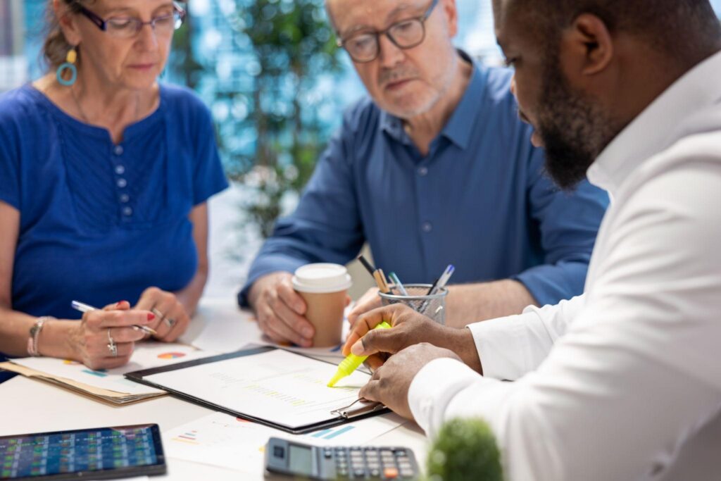 Group of professionals collaborating at a table with documents, pens, a coffee cup, and a calculator at a bright office.