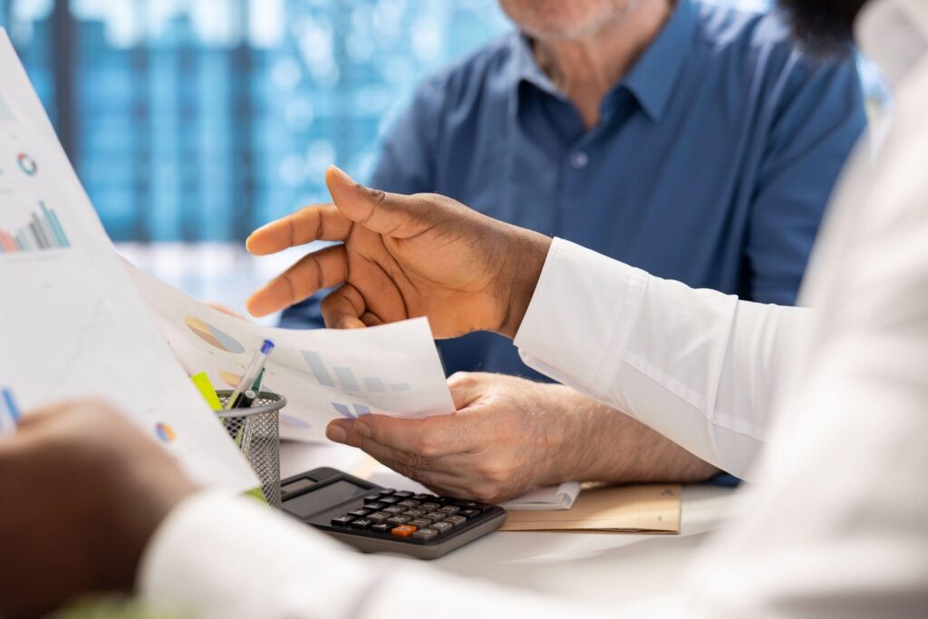 What Are the Reporting Requirements for a Bare Trust - Advanced Tax Services Two people at a desk reviewing printed charts and a calculator during a business meeting.